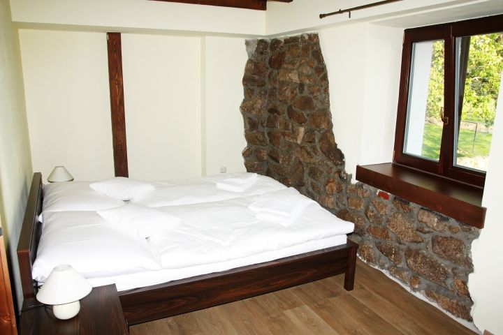 pohled na postel ve dvoulůžkovém pokoji s kamennou stěnou